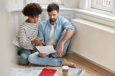 Imagem de um casal discutindo documentos financeiros em casa, destacando a importância de itens essenciais para o primeiro lar, como aquecedor solar, por que investir neste item.