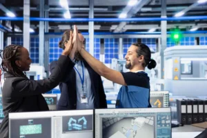 Equipe de profissionais em fábrica de manufatura colaborativa global celebrando sucesso no projeto de cloud industrial, destacando eficiência e inovação industrial
