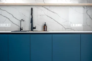 Imagem de uma cozinha moderna com cuba e torneira preta, bancada branca e portas de armário de PVC azul, ideal para quem busca como escolher porta de PVC para armário de pia