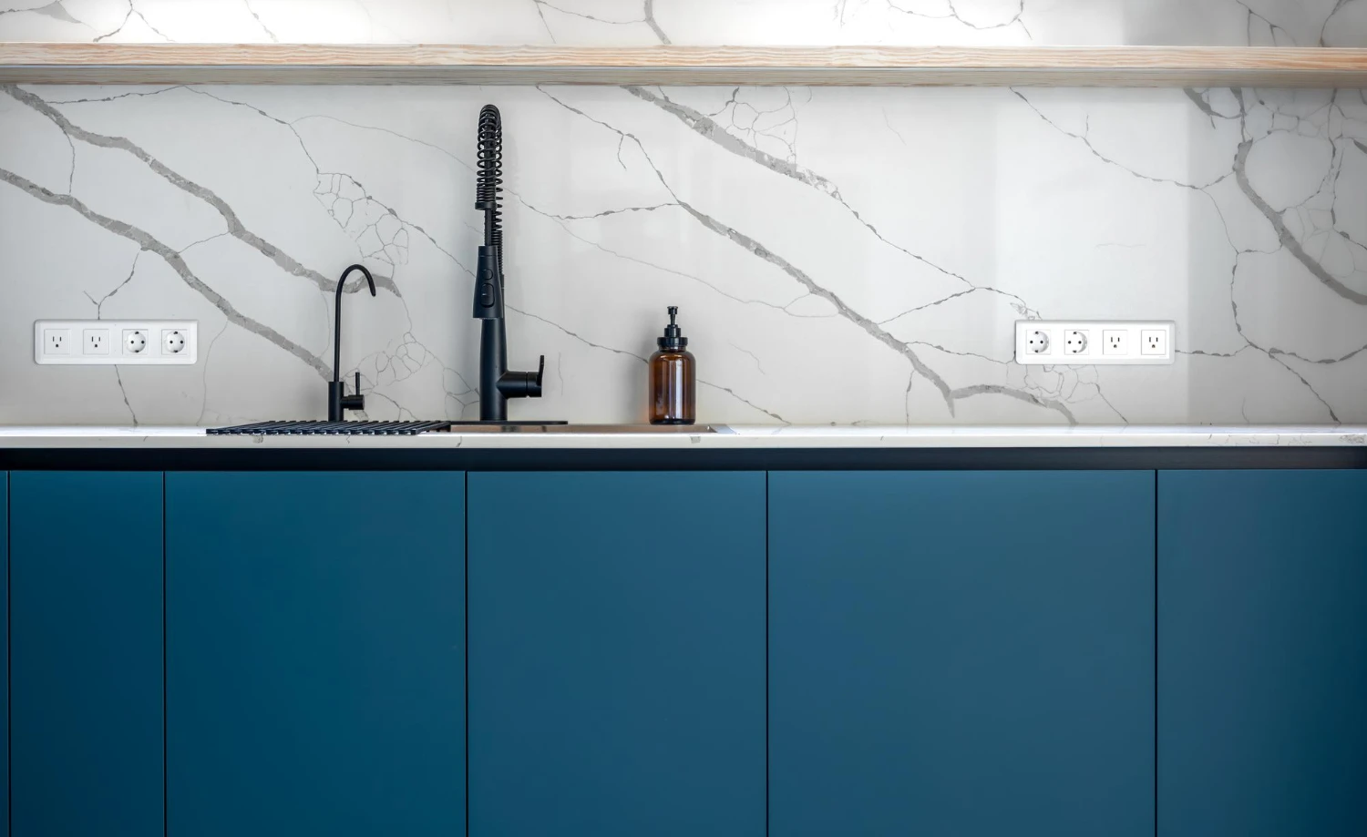 Imagem de uma cozinha moderna com cuba e torneira preta, bancada branca e portas de armário de PVC azul, ideal para quem busca como escolher porta de PVC para armário de pia