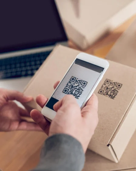 Pessoa usando smartphone para escanear QR code em embalagem inteligente, destacando rastreamento e experiência do cliente com tecnologia moderna.