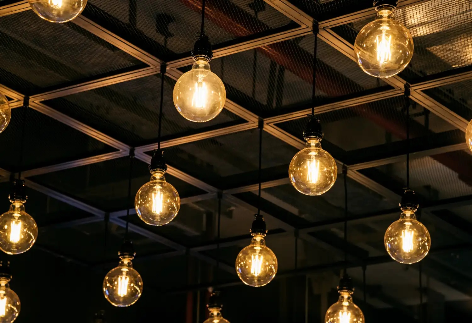 Iluminação estilo Industrial: Pendentes, trilhos e lâmpadas que fazem a diferença: Iluminação estilo Industrial: Pendentes, trilhos e lâmpadas com design em vidro e filamento exposto, penduradas em estrutura metálica quadriculada, criando efeito acolhedor em ambiente interno.