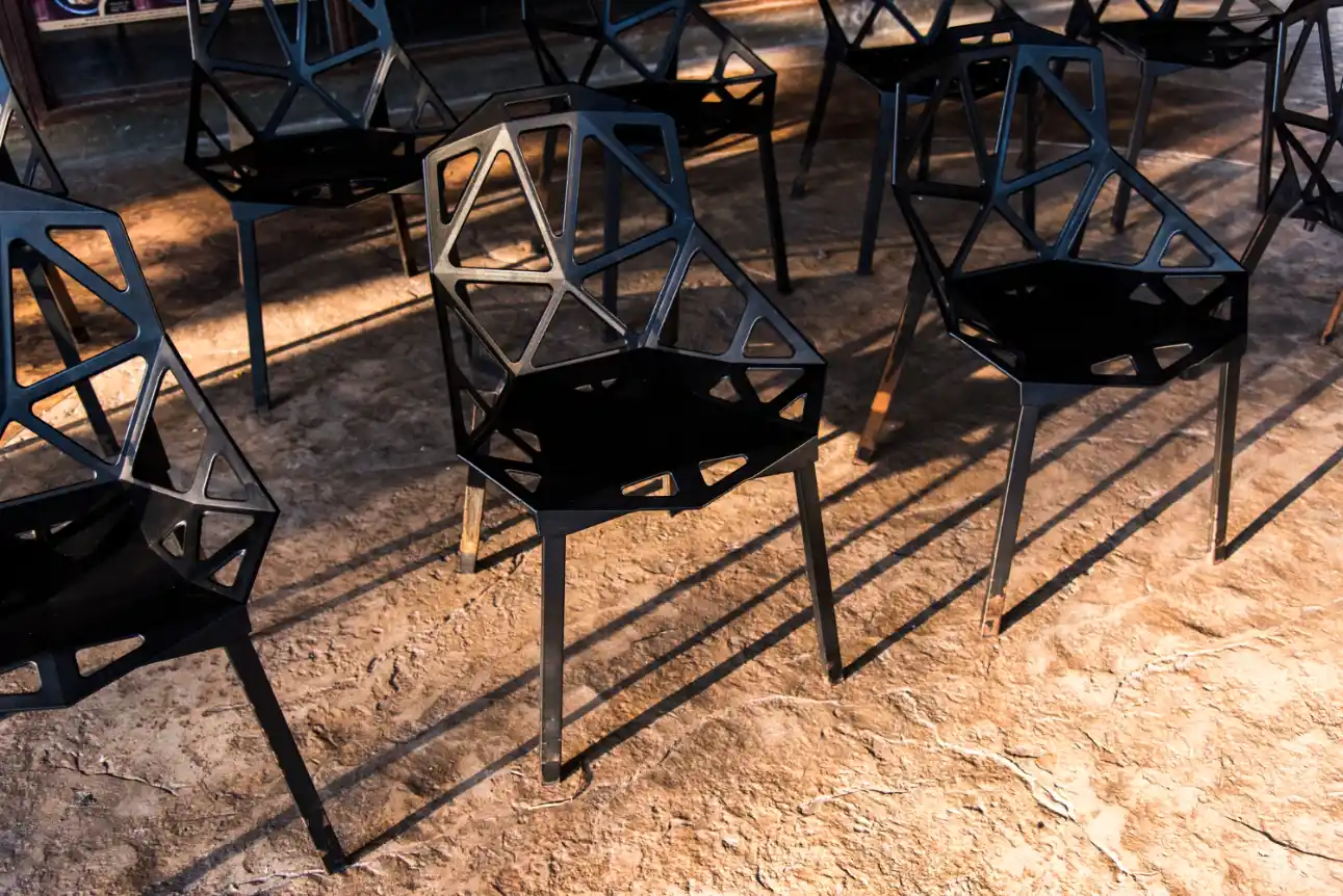Móveis de estilo Industrial: Como escolher peças de metal e madeira de demolição: Conjunto de cadeiras e mesas com estrutura de metal em design geométrico, apoiadas sobre piso de concreto queimado, estilo industrial com aparência robusta.