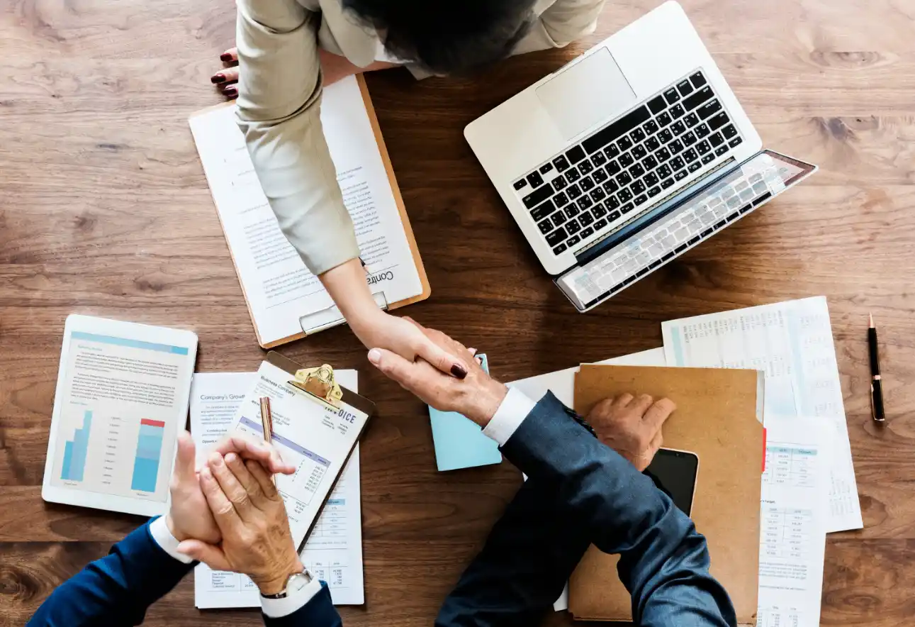 Self-Attribution: Como Implementar uma Pesquisa Simples para Descobrir Como o Cliente Realmente Chegou Até a Marca: Profissionais analisando relatórios e planilhas em uma mesa de escritório, com um notebook e gráficos abertos durante reunião para discutir dados de marketing e clientes.